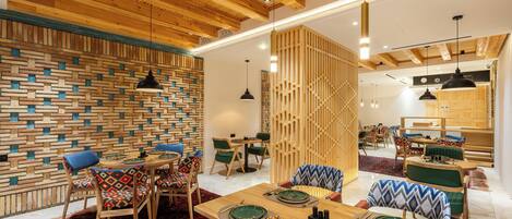 A modern dining area with wooden ceiling beams, a patterned wall, and a mix of wooden and upholstered chairs.