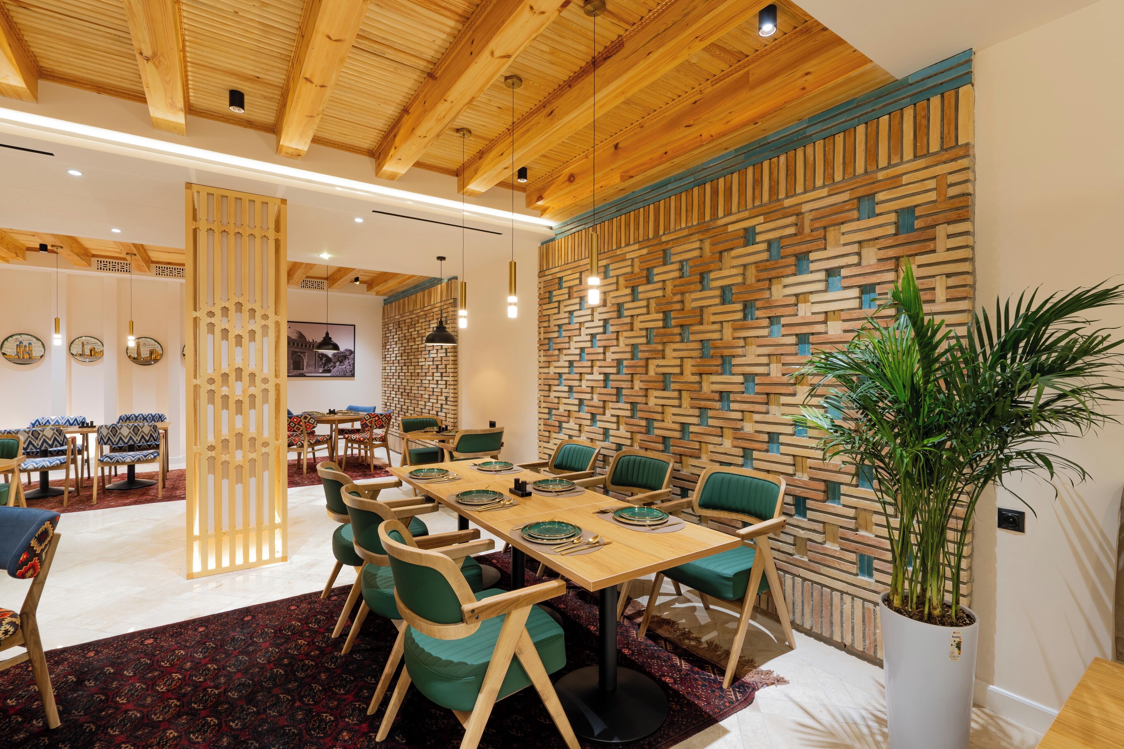 Un espace repas moderne avec un plafond en bois, un mur décoré d’un motif en briques et des chaises recouvertes d’un tissu vert.