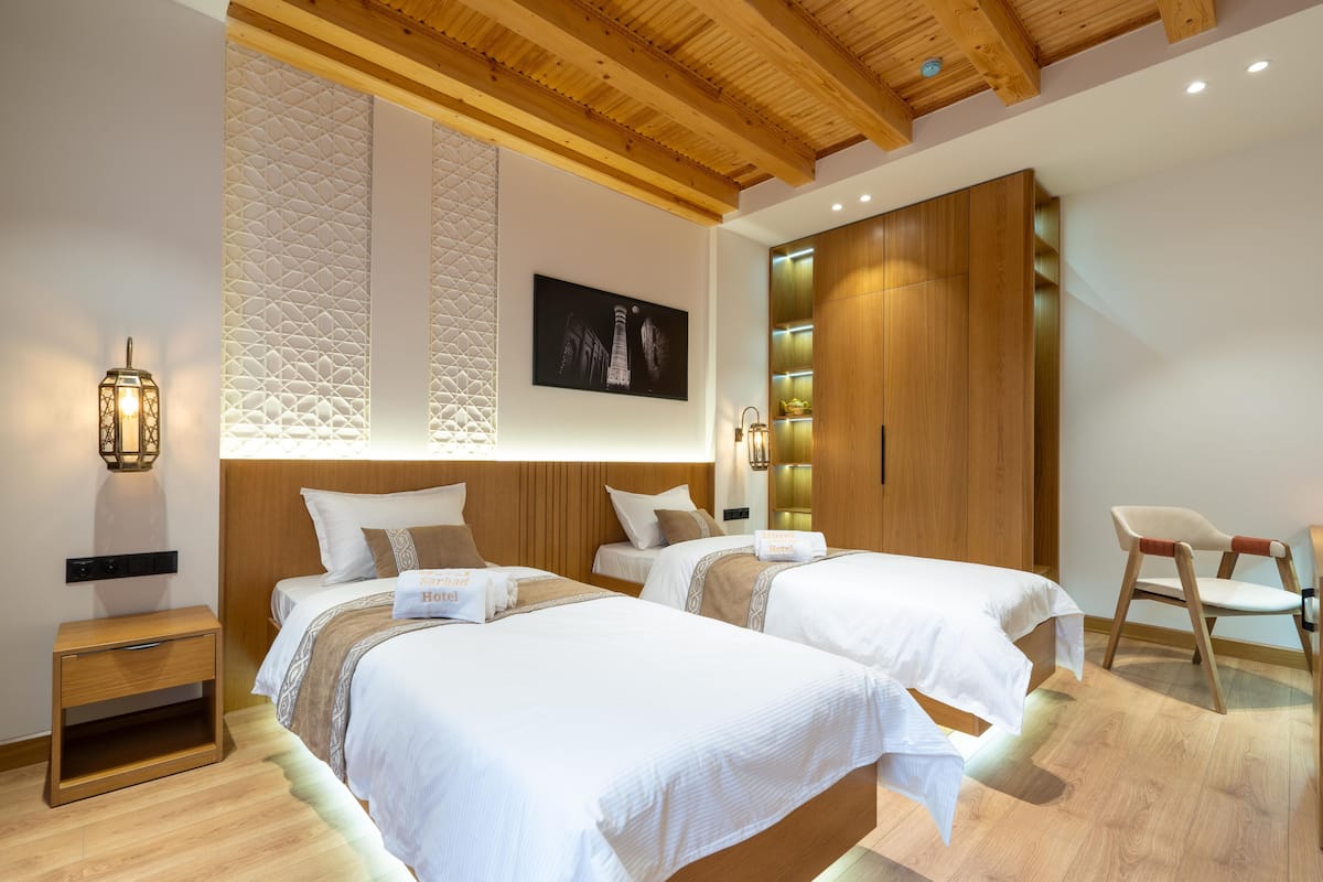 A hotel room with two beds, a wooden ceiling, a wall-mounted artwork, and a nightstand.