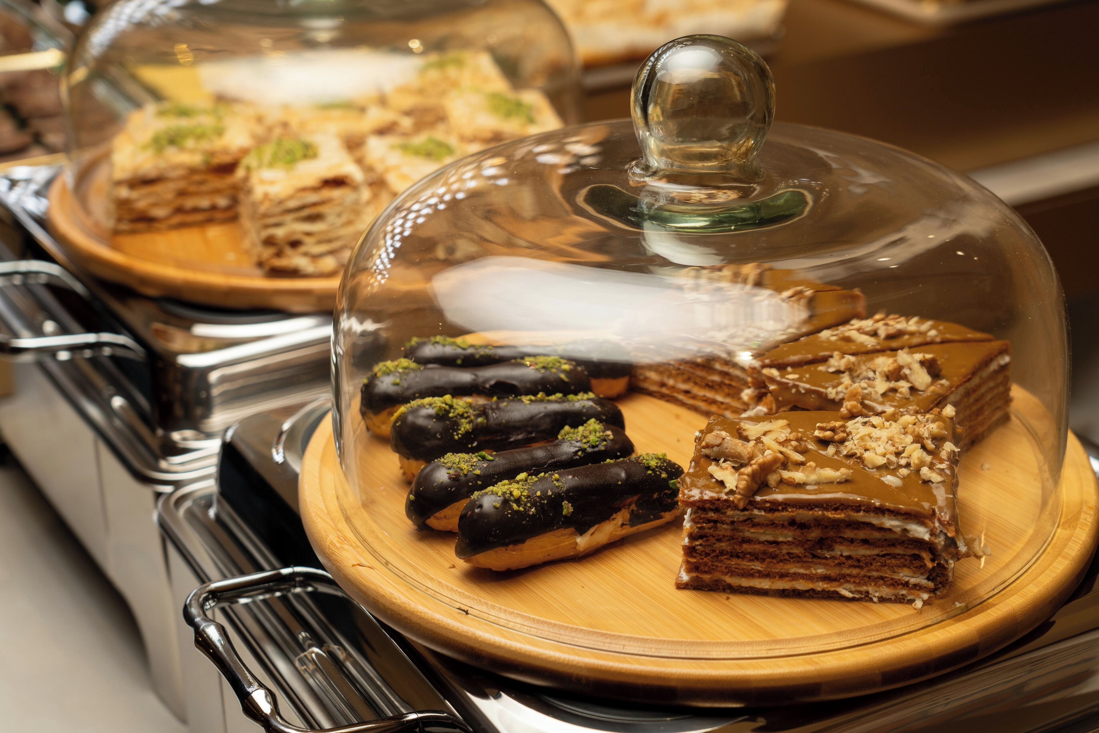 Un bufé con diversos postres bajo campanas de cristal, incluyendo pasteles bañados en chocolate y un pastel en capas.