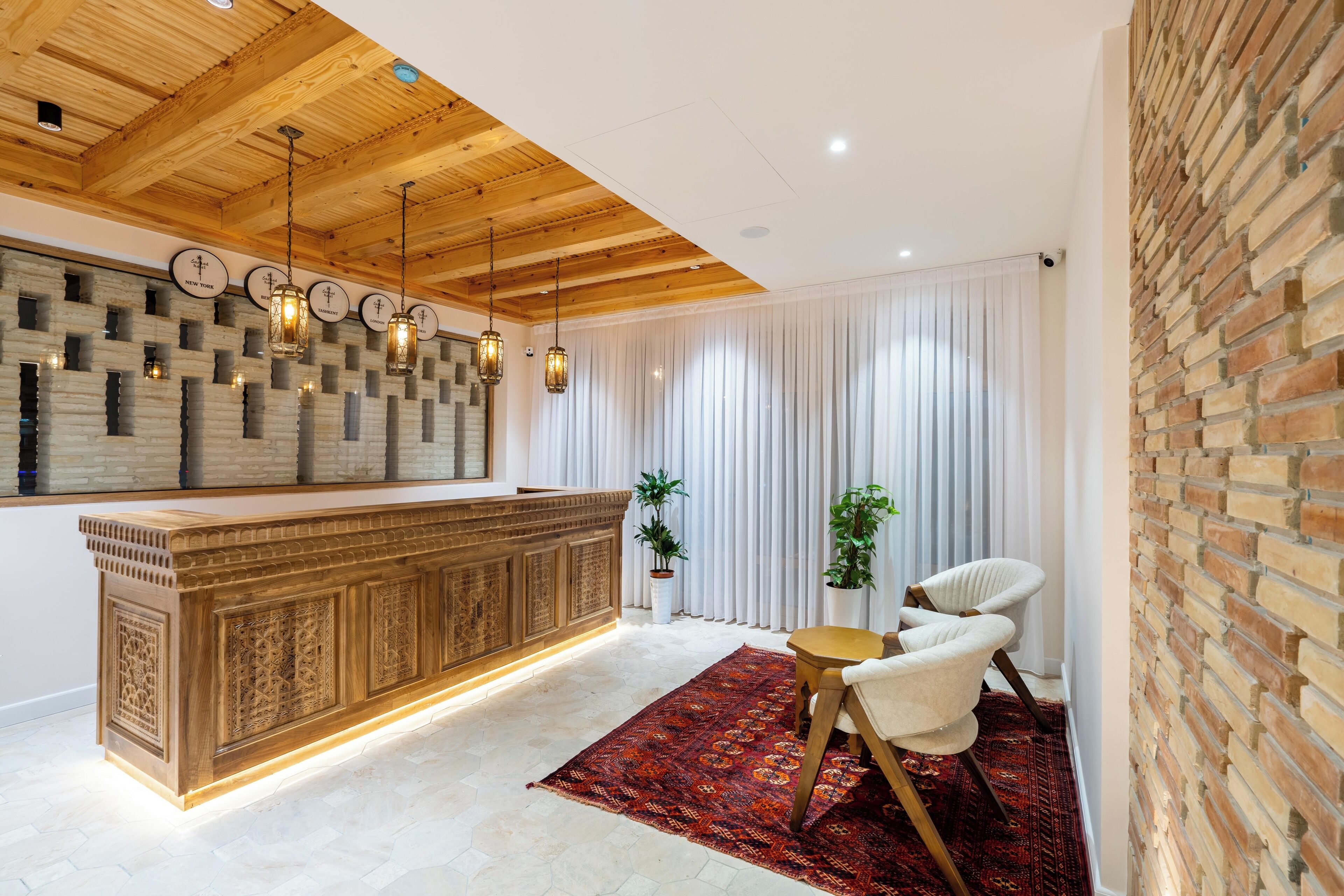 Un intérieur moderne avec un plafond en bois, un mur à motifs, un comptoir d’accueil, un tapis rouge et deux chaises.