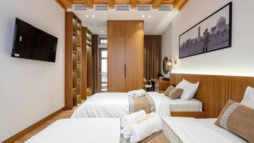 A hotel room with two beds, a TV, wooden paneling, a cityscape painting, and a desk with a lamp.