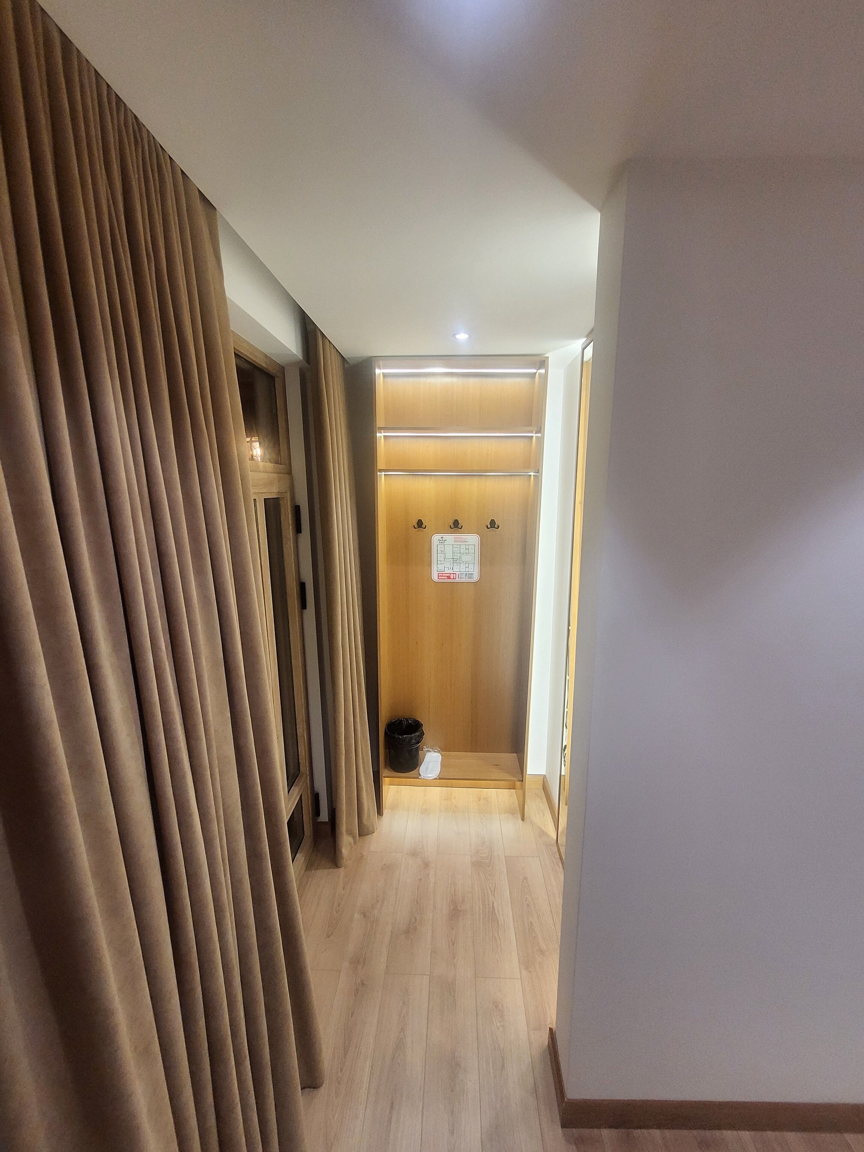Un pasillo con suelo de madera, una puerta de madera y un letrero, y un basurero negro.
