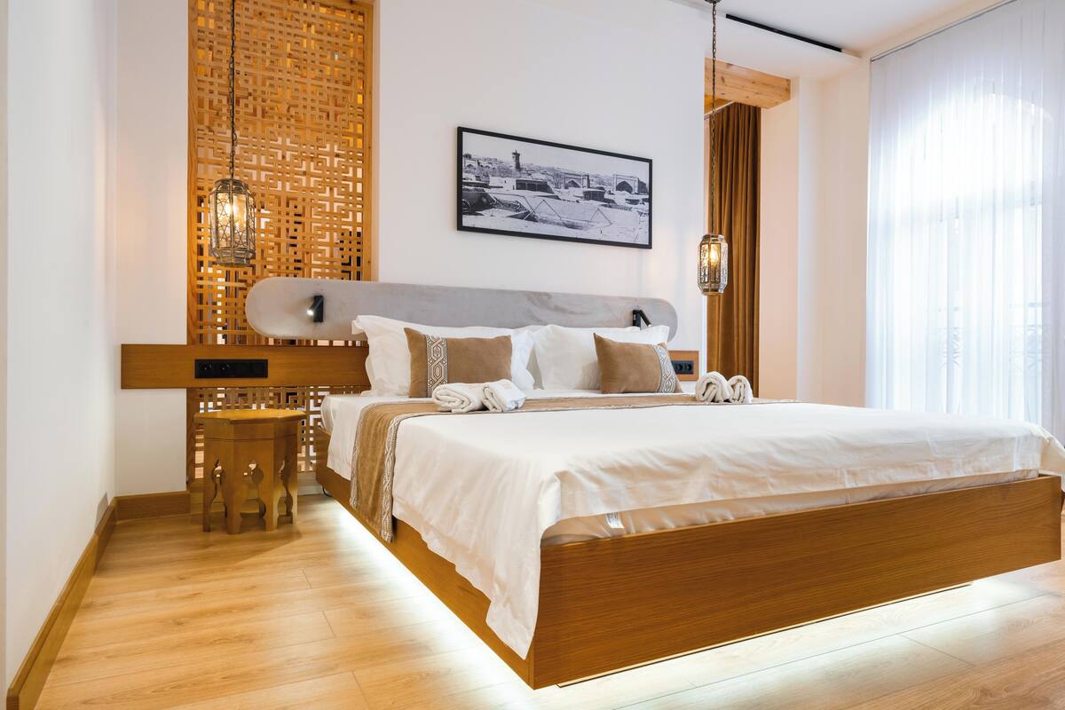 A modern bedroom with a wooden bed frame, a wooden nightstand, a wall-mounted light fixture, and a framed picture on the wall.