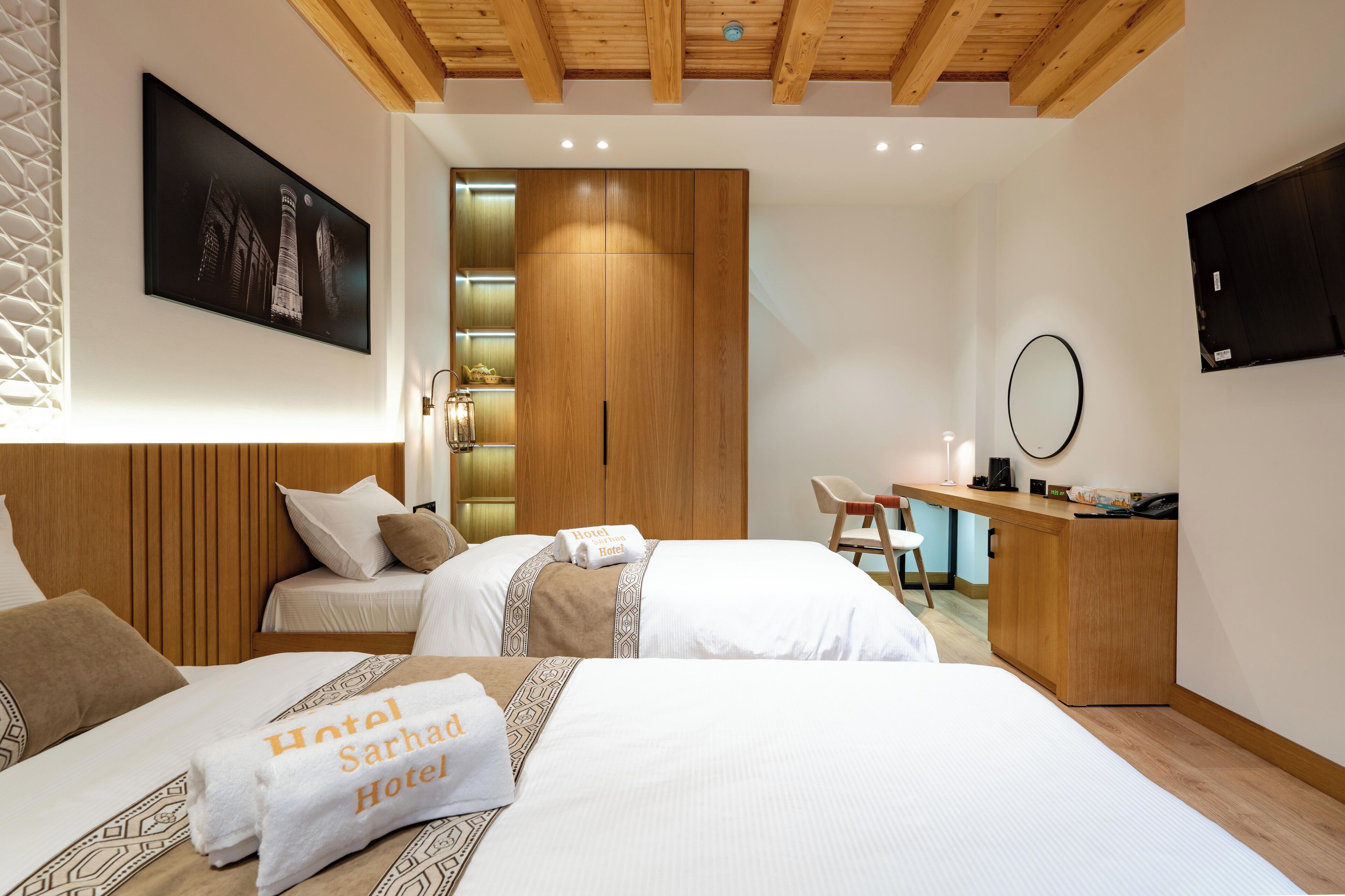 A hotel room with two beds, a desk, a wardrobe, and a TV.