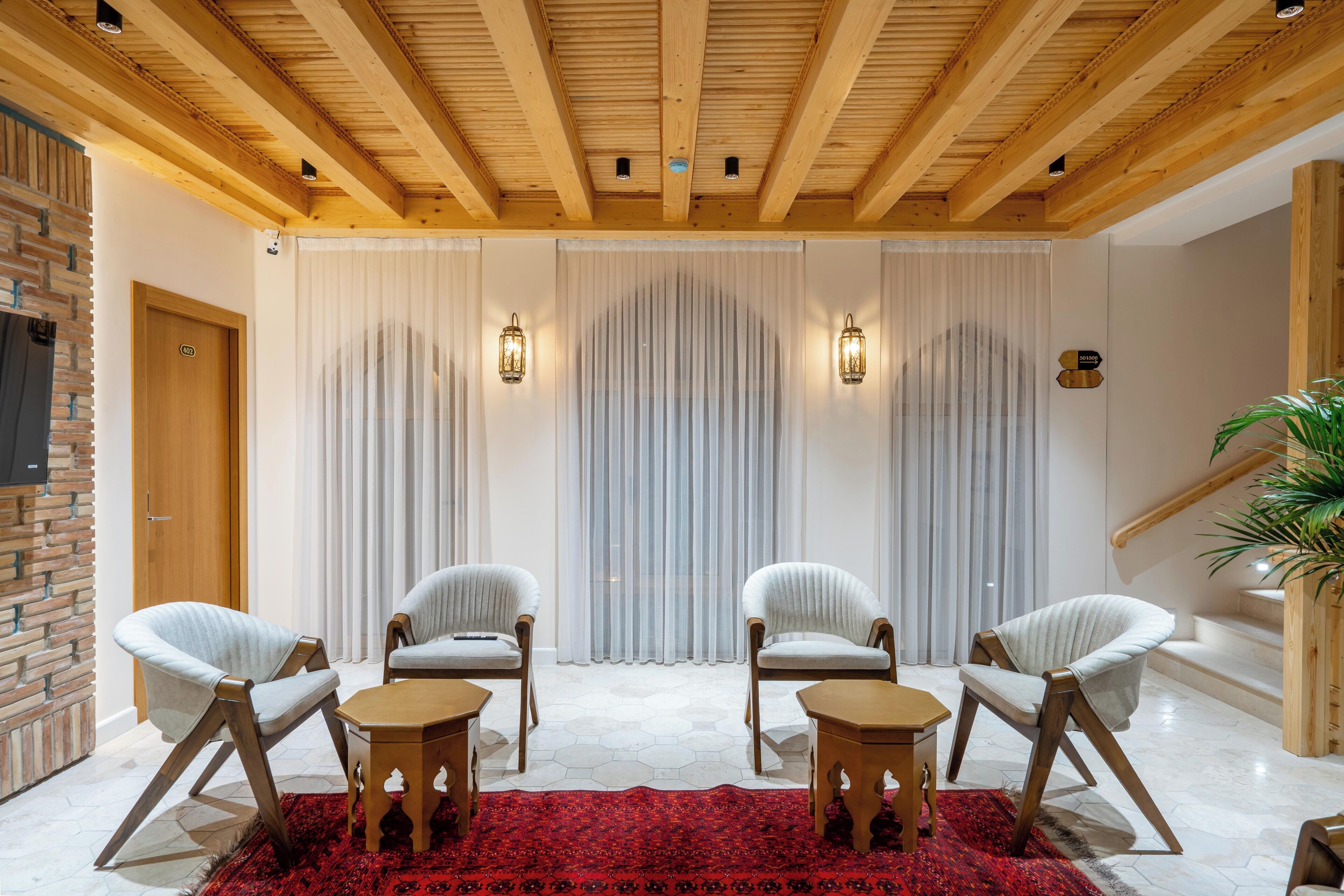 Una habitación con cuatro sillones blancos, un tapete rojo estampado, mesas de madera y techo de madera.