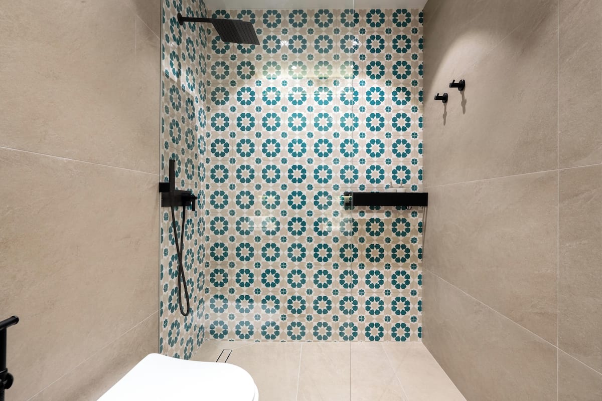A bathroom with a patterned tile wall, a shower area, and a toilet.