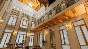 A spacious interior with high ceilings, large windows, and a balcony with wooden railings. - Sarhad Hotel (Bukhara)