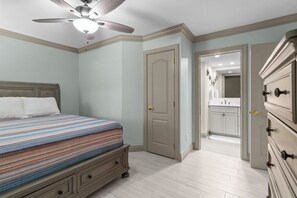 Un dormitorio con cama, ventilador de techo, puerta y cómoda.