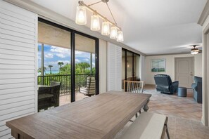 A spacious balcony with a wooden table and chairs, a ceiling light fixture, and a view of the ocean.