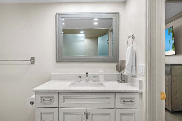 Un baño con un lavamanos, espejo y armarios blancos.