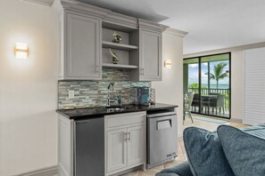 A modern kitchen with grey cabinets, a black countertop, and a view to a balcony with outdoor furniture.