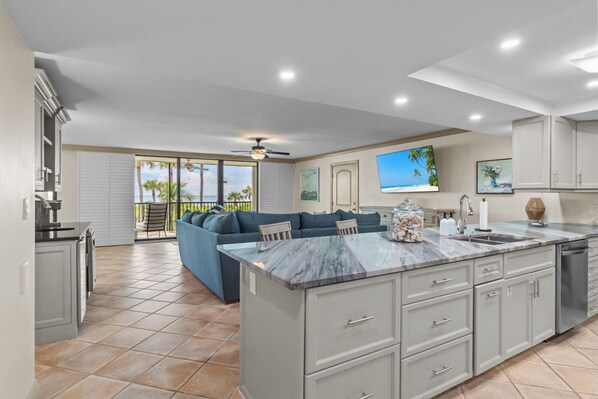 A spacious kitchen with a large island, a dining area with a blue sofa, and a view of the outdoors through a sliding glass door.