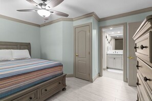 A bedroom with a bed, a ceiling fan, a door, and a dresser.