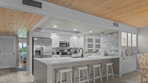 A modern kitchen with white cabinetry, a central island with stools, and a wooden ceiling.