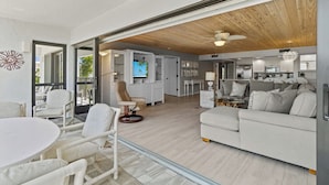 A spacious living area with a white sofa, a round table, and a TV in the background.