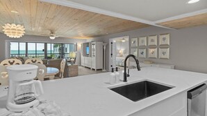 A modern kitchen with a white countertop, black sink, and a coffee maker.