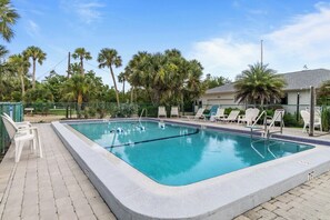 Una piscina rectangular con solárium empedrado, rodeada de palmeras y sillones de descanso.