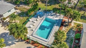 An aerial view of a residential property with a rectangular swimming pool surrounded by lounge chairs and palm trees.