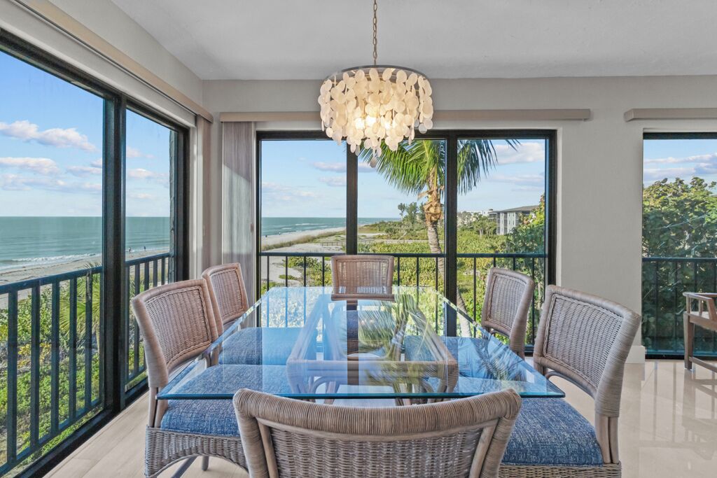 Een eetruimte met een glazen tafel en rieten stoelen, met uitzicht op een strand en zee.