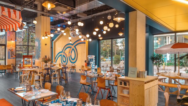 A restaurant interior with tables set for dining, a large mural on the wall, and hanging pendant lights. - Eklo Hotels Nantes City center - Île de Nantes (Nantes)