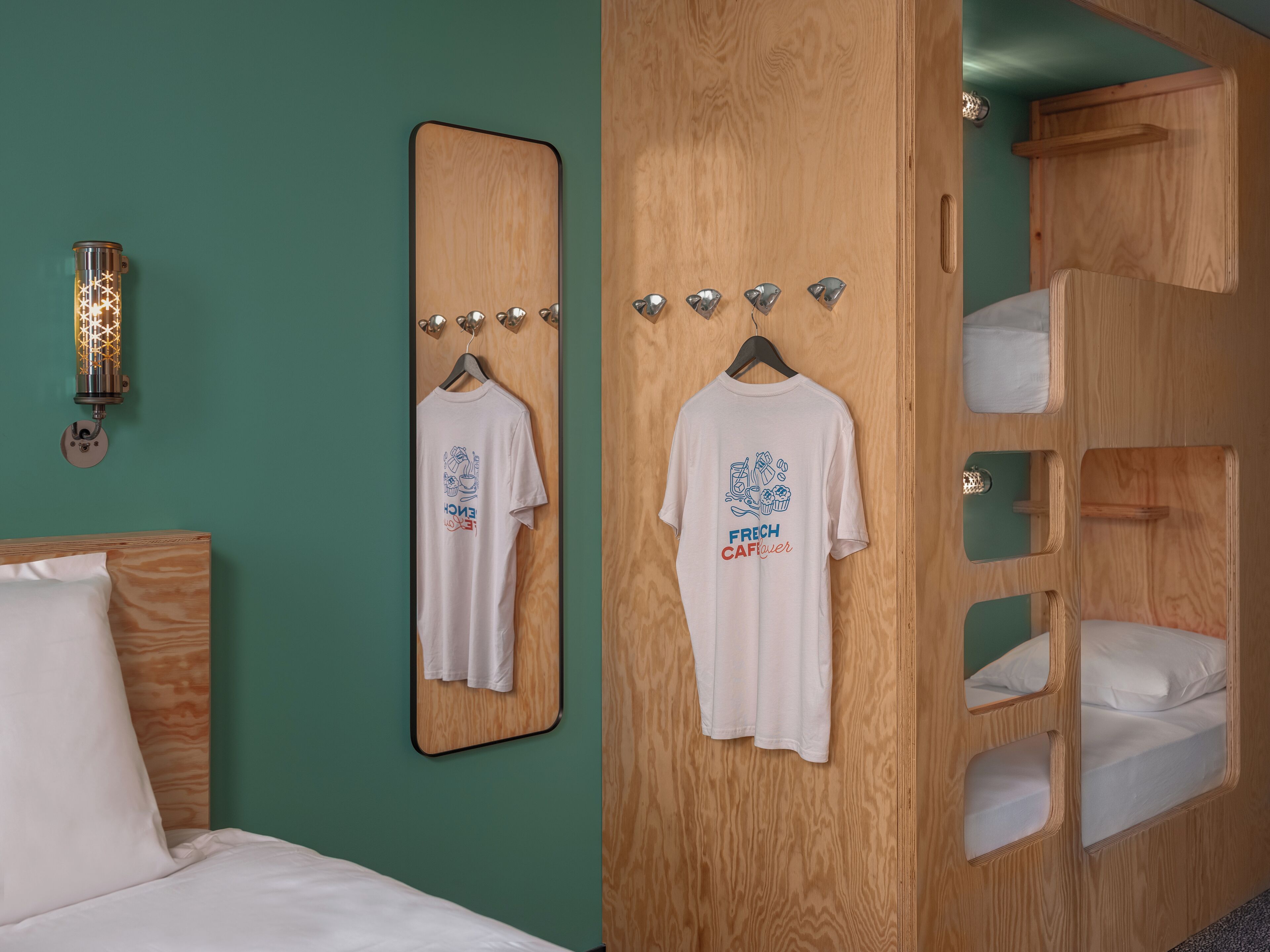A hotel room with a bed, a mirror, a wardrobe with hangers, and a bunk bed.