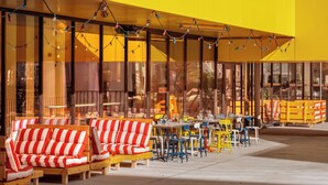 A yellow building with outdoor seating, including striped sofas and tables, and a covered area with string lights. - Eklo Hotels Nantes City center - Île de Nantes (Nantes)