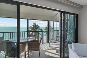 A balcony with a glass door, a round table with wicker chairs, and a view of the ocean. - Gulf-Front Escape with Private Rooftop Sundeck & Sweeping Sunset Views (Sanibel)