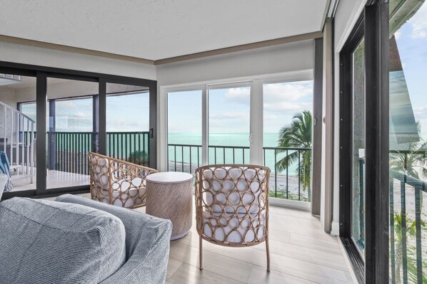 A balcony with a view of the ocean, wicker furniture, and a sliding glass door. - Gulf-Front Escape with Private Rooftop Sundeck & Sweeping Sunset Views (Sanibel)