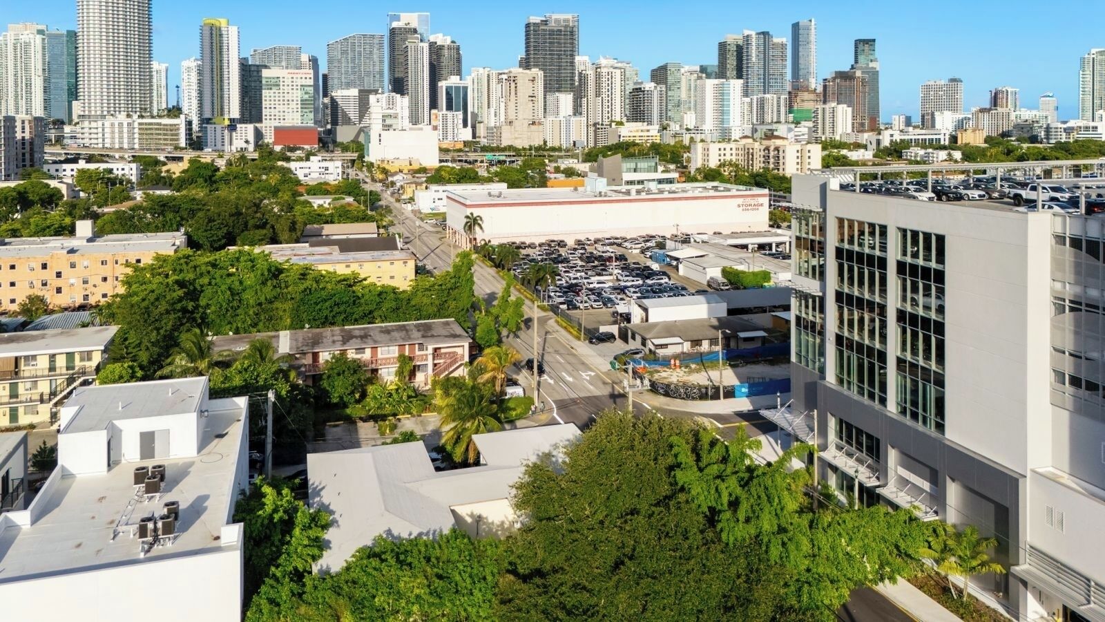 A cityscape with high-rise buildings, a parking lot, and a large storage facility.