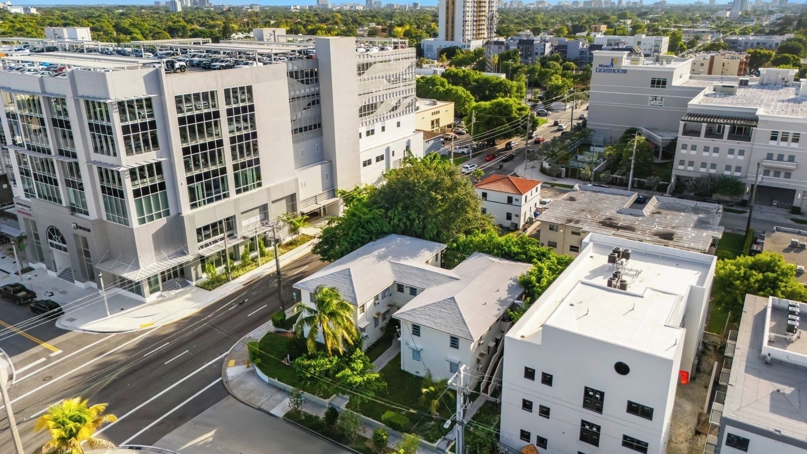 Un quartier urbain moderne qui présente un mélange de bâtiments résidentiels et commerciaux, notamment un immeuble de bureaux imposant doté de grandes fenêtres et d’un parking.