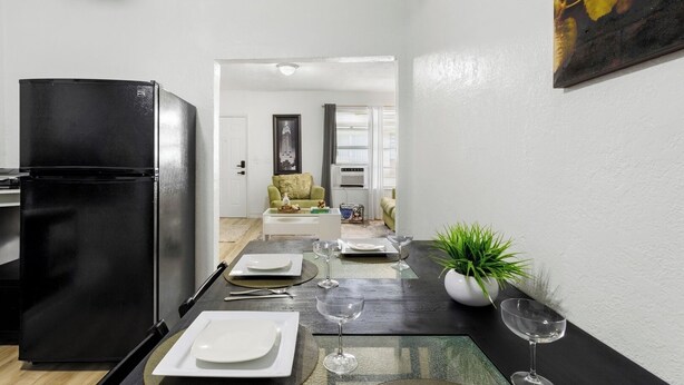 A compact kitchen with a black refrigerator, a dining table set with plates and wine glasses, and a potted plant on the right. - Pet-friendly Brickell Stay Near Beach & City (Miami)