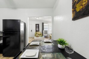 A compact kitchen with a black refrigerator, a dining table set with plates and wine glasses, and a potted plant on the right. - Pet-friendly Brickell Stay Near Beach & City (Miami)