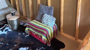 L’intérieur chaleureux d’un chalet avec un plafond en bois, un tableau représentant un paysage, un tapis en peau de vache et une couverture colorée.
