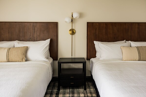 A hotel room with two beds, a nightstand with a lamp, and a checkered floor. - The Vic (Traverse City)