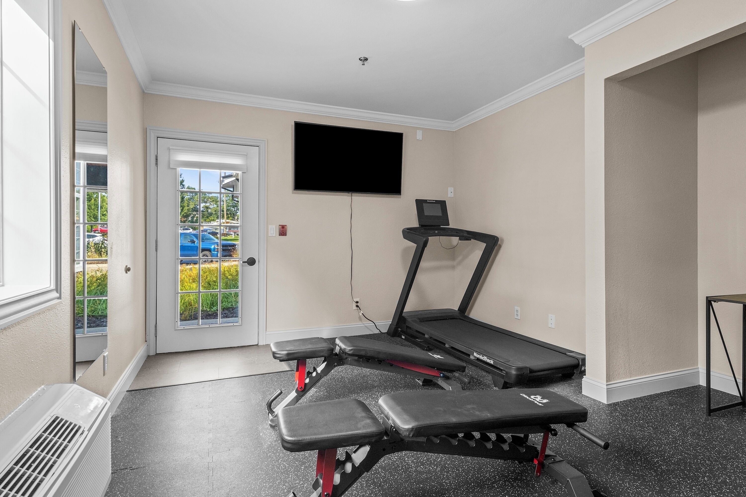 Une salle de sport à domicile équipée d’un tapis de course, d’un banc de musculation et d’un téléviseur fixé au mur.