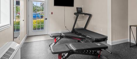 Une salle de sport à domicile équipée d’un tapis de course, d’un banc de musculation et d’un téléviseur fixé au mur.