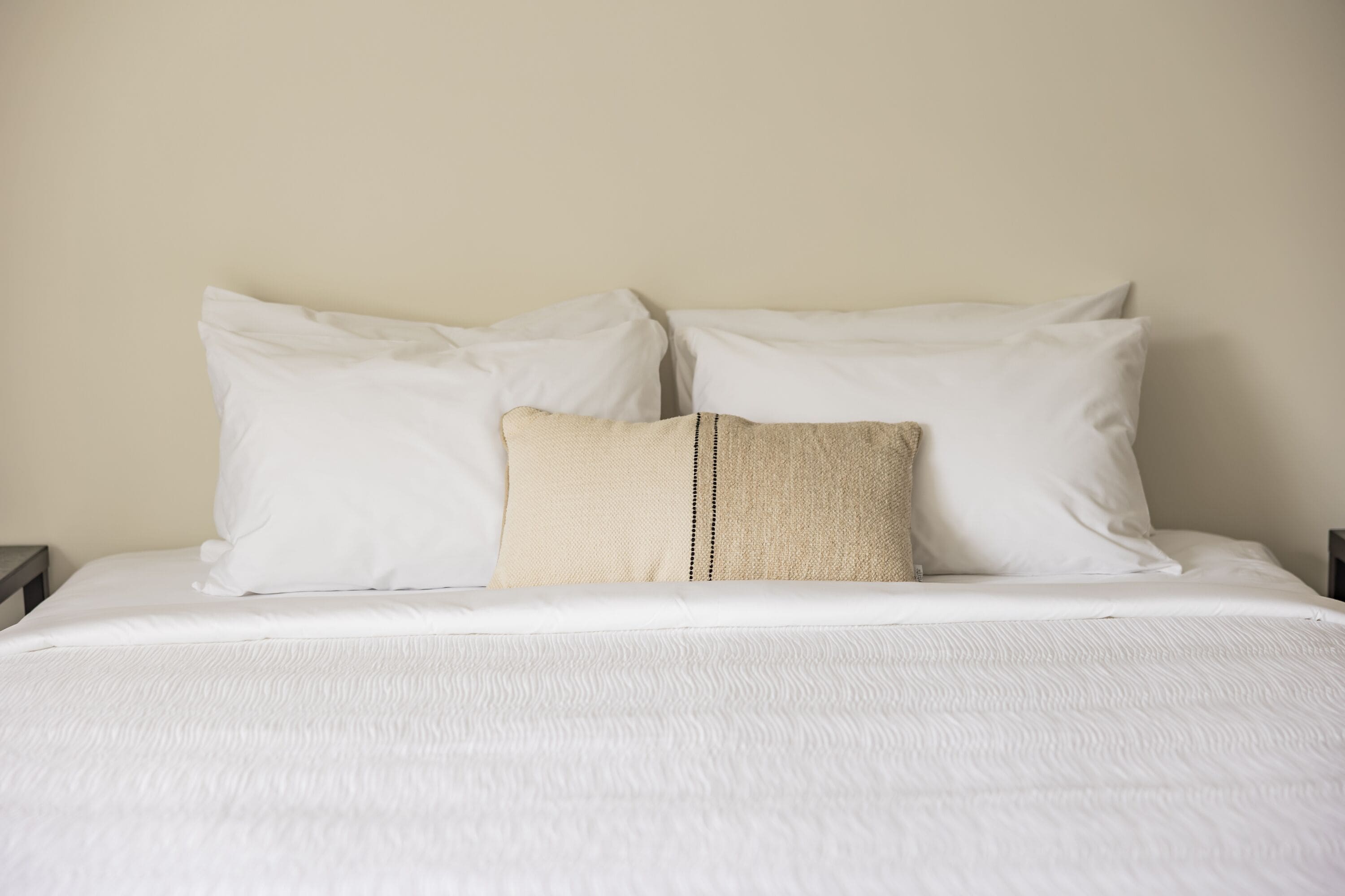A neatly made bed with white bedding and a beige pillow.