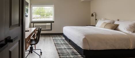 A bedroom with a bed, a desk, a chair, and a window.
