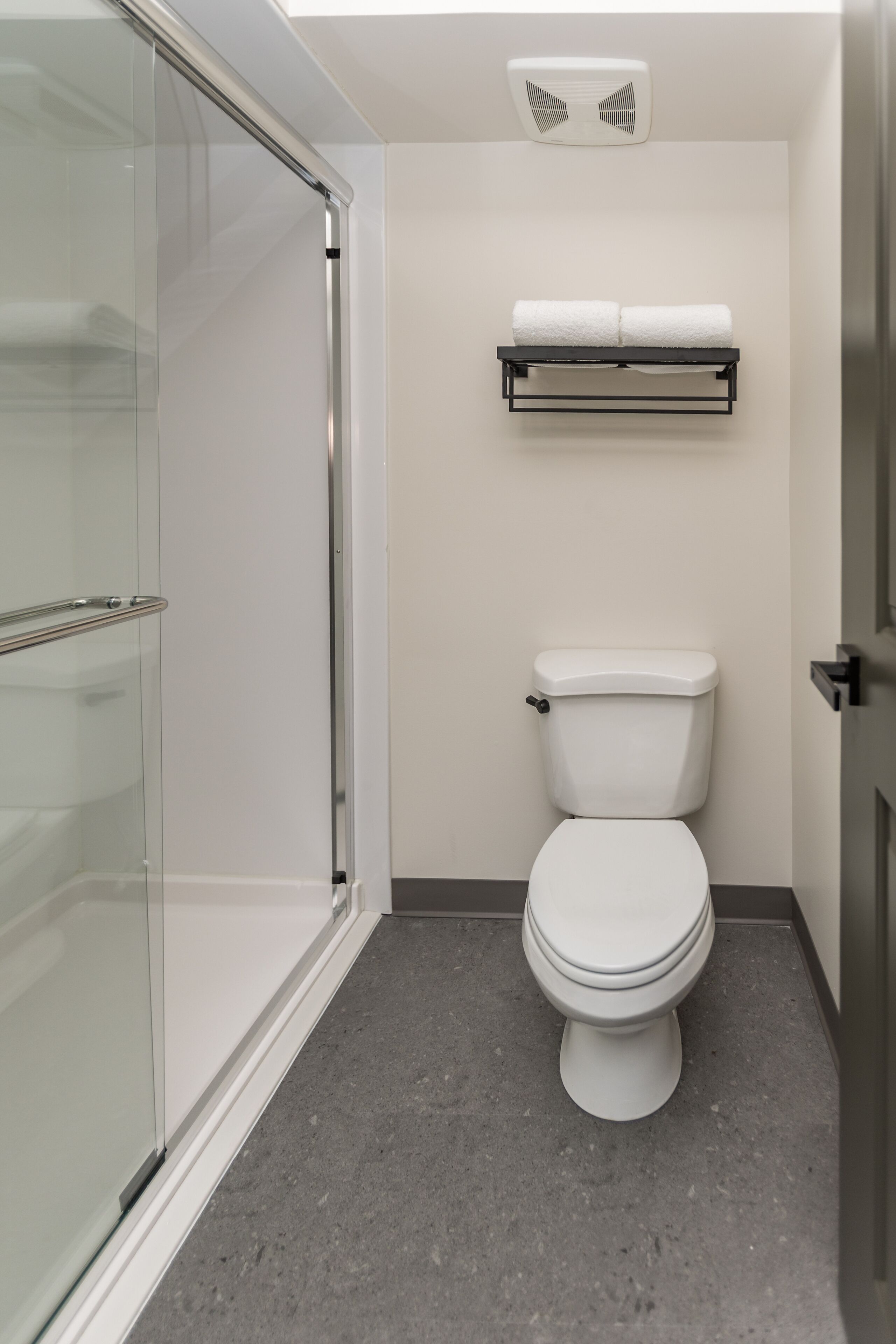 Un baño moderno con cabina de ducha de vidrio, un inodoro blanco y un perchero para toallas.