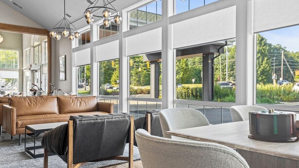 Ein modernes Wohnzimmer mit einer Ledersofa, einem Esstisch und einem großen Fenster mit Blick ins Freie.