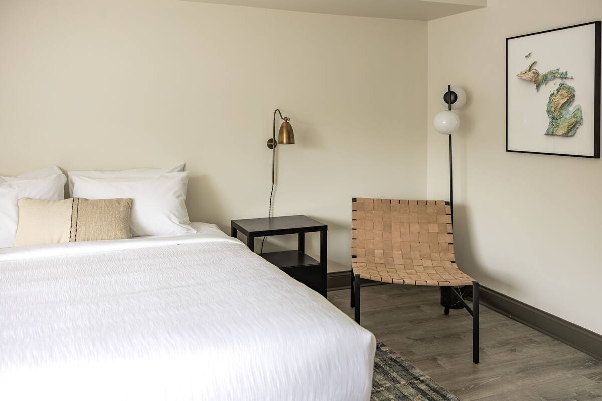 Ein Hotelzimmer mit einem großen Bett, einem kleinen Tisch, einem Stuhl, einer Lampe und einer gerahmten Karte an der Wand.