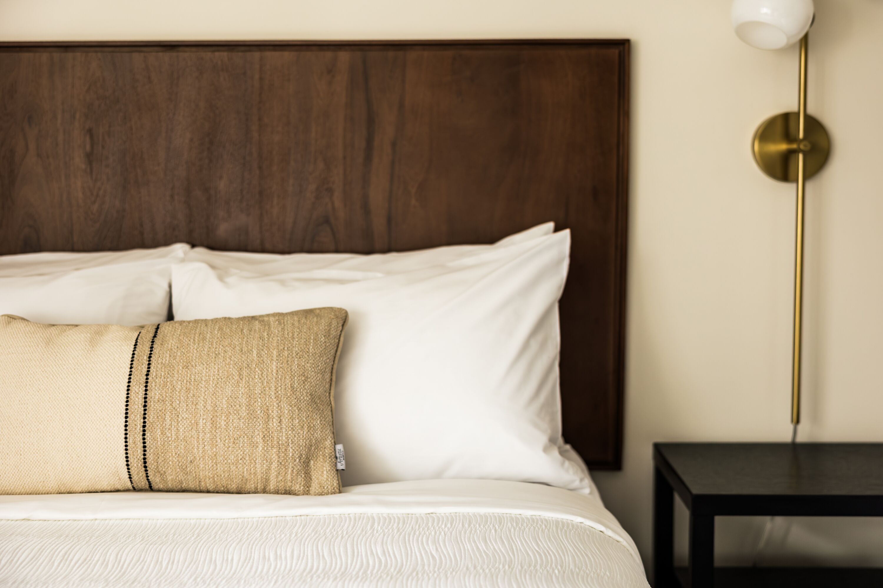 Una cama bien hecha con sábanas blancas y dos almohadas, una de ellas con textura color beige.