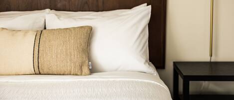 Una cama bien hecha con sábanas blancas y dos almohadas, una de ellas con textura color beige.
