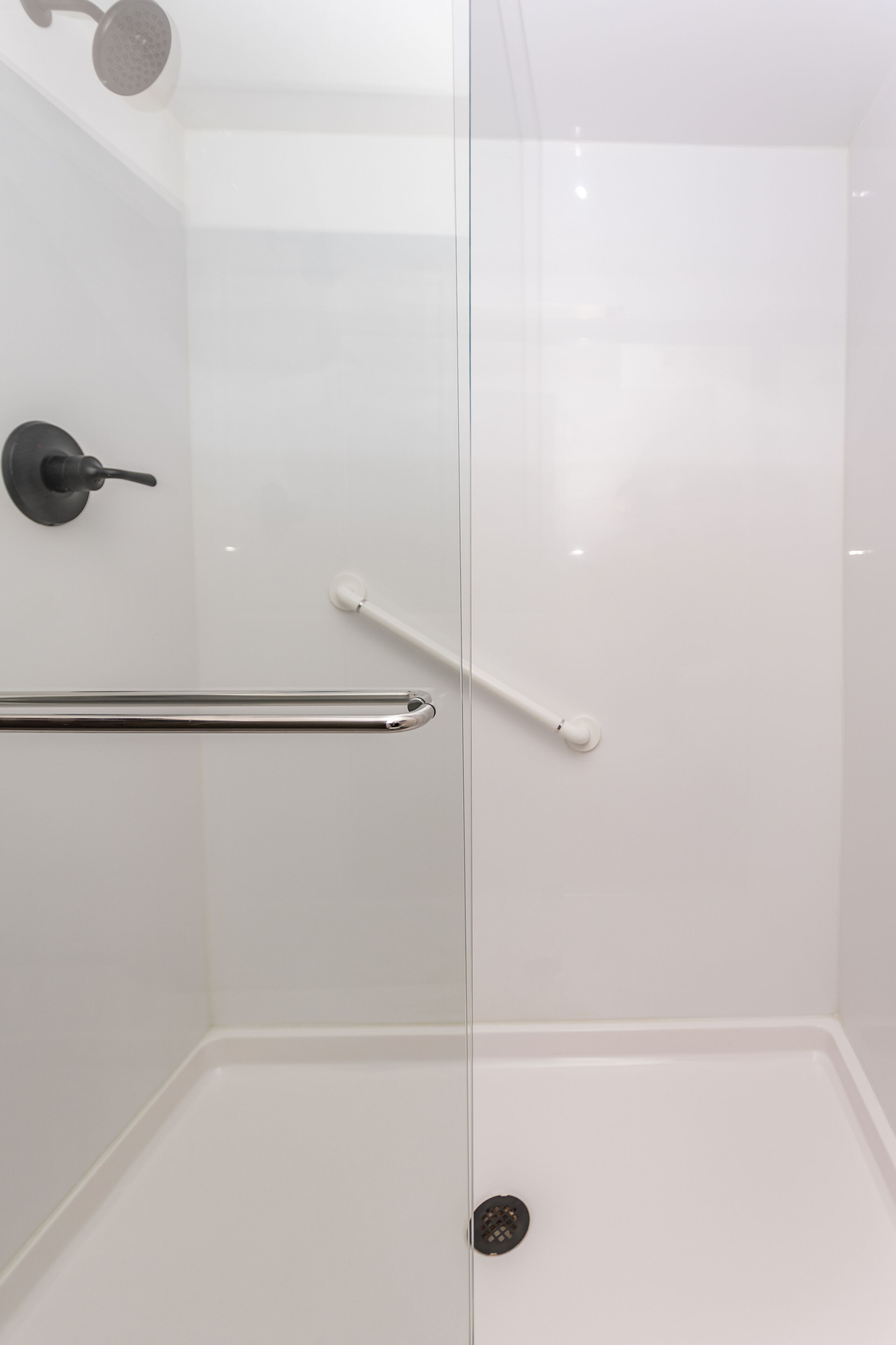 Eine moderne Dusche mit Glastür, Handlauf und Duschkopf.