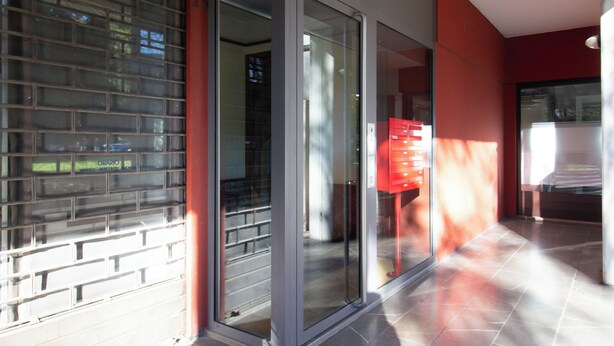 A modern building with a glass door entrance, a red mailbox, and a tiled floor.