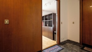 A hotel entrance with a wooden door, a welcome mat, and a view into a room with a kitchenette.