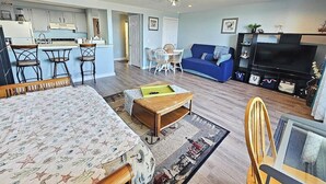 A living room with a sofa, a coffee table, a TV, and a dining area with chairs. - Beachfront Condo with Amazing Ocean Views  4th Fl (Old Orchard Beach)
