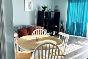 Un comedor con una mesa redonda de madera, sillas blancas, un mueble de entretenimiento negro y una cortina azul.