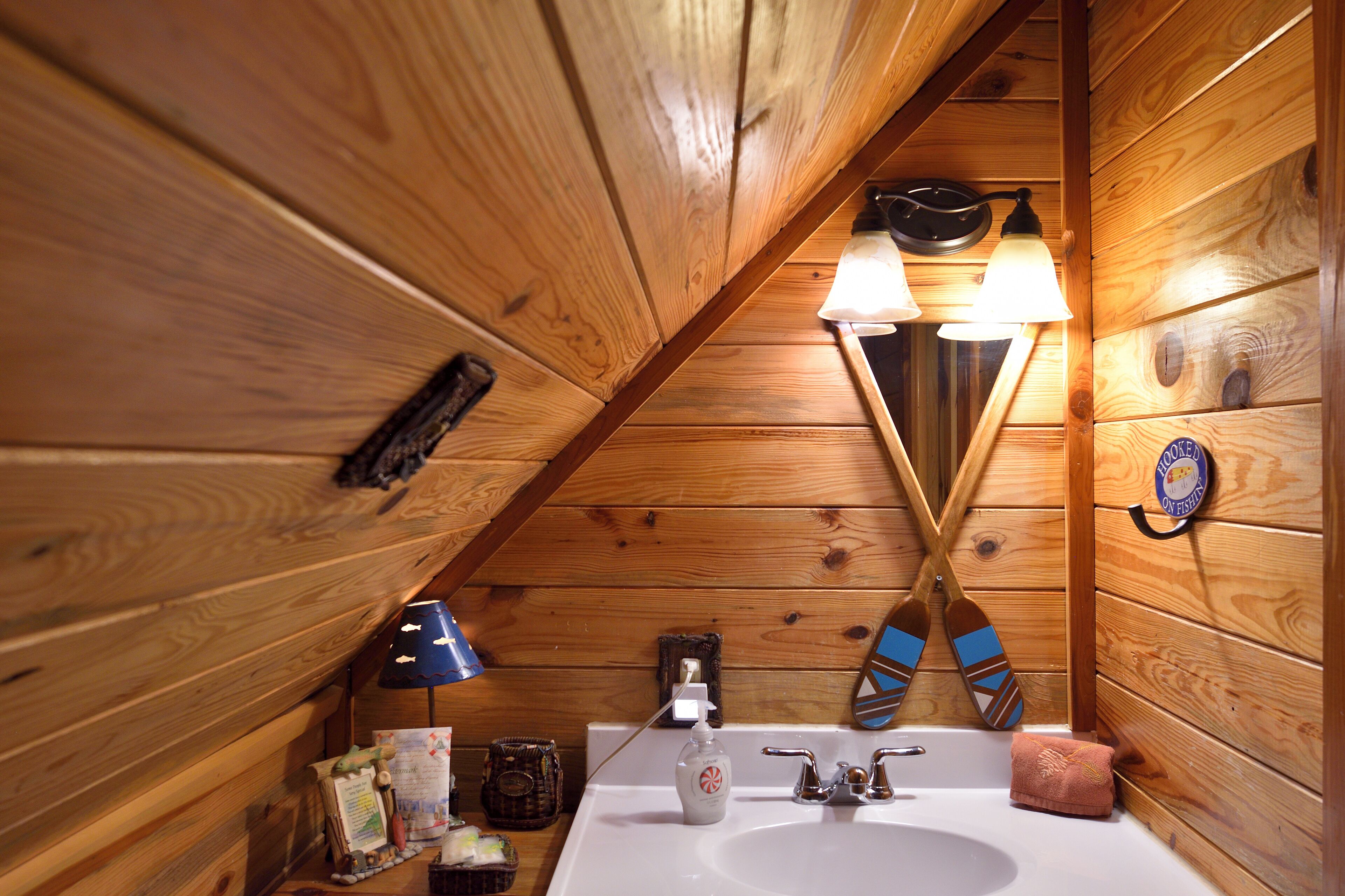 Un baño de cabaña de madera con un lavabo, dos luces empotradas, un espejo y una toalla.